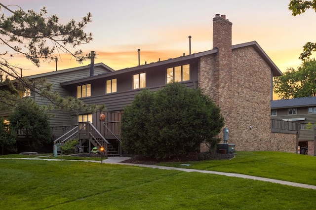 123 Windsor Ct, New Brighton, MN 55112 - back of house at dusk with stairway, a yard, central AC unit, and a chimney