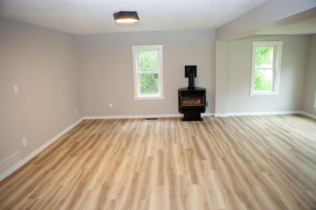 213 Lake Ave, Detroit Lakes, MN 56501 - unfurnished living room with a wood stove, plenty of natural light, light wood-style floors, baseboards, and a textured ceiling
