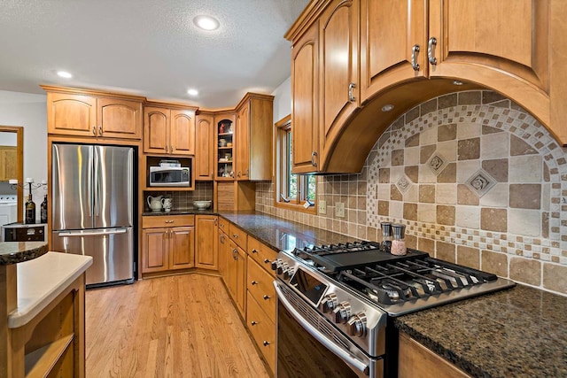 13545 Glasgow Ln, Apple Valley, MN 55124 - kitchen featuring appliances with stainless steel finishes, light wood-style flooring, brown cabinetry, open shelves, and dark stone counters