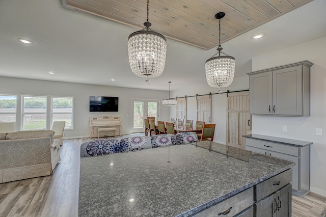 17690 Clayton Ave E, Vermillion Twp, MN 55068 - kitchen with a chandelier, gray cabinetry, a barn door, dark stone counters, and light wood-type flooring