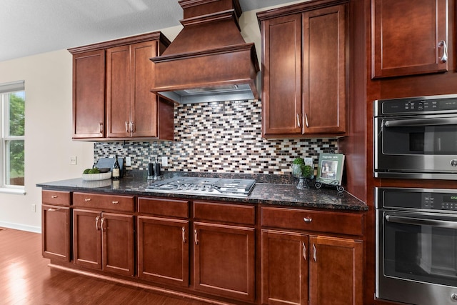 14111 Abercorn Ave, Rosemount, MN 55068 - kitchen featuring premium range hood, stainless steel appliances, wood finished floors, decorative backsplash, and dark stone countertops
