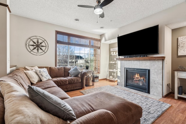 6665 Flycatcher Ln, Apple Valley, MN 55124 - living area featuring ceiling fan, wood finished floors, a tiled fireplace, a textured ceiling, and baseboards