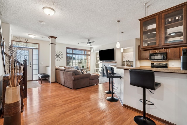 6665 Flycatcher Ln, Apple Valley, MN 55124 - kitchen with black microwave, range, light wood-style floors, a textured ceiling, and a kitchen breakfast bar