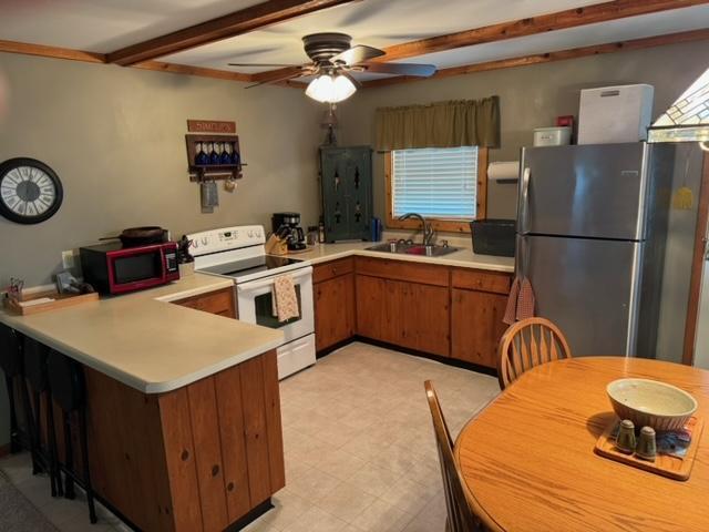 48408 Pillar Rd, Deer River, MN 56631 - kitchen featuring white range with electric stovetop, freestanding refrigerator, a sink, a peninsula, and brown cabinetry