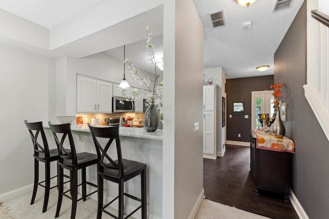 2244 Water Lilly Ln Unit 405, Eagan, MN 55122 - kitchen with a kitchen bar, stainless steel microwave, white cabinets, baseboards, and a textured ceiling