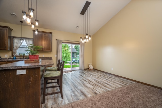 411 Ladd Ln, Osceola, WI 54020 - kitchen with lofted ceiling, dark countertops, dark brown cabinets, a kitchen breakfast bar, and decorative light fixtures