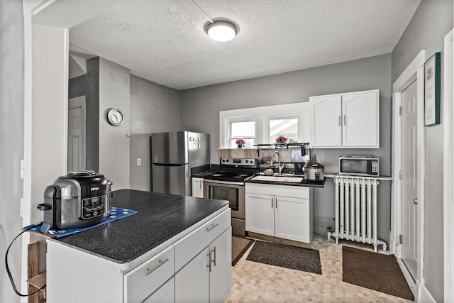 2745 Columbus Ave, Minneapolis, MN 55407 - kitchen with radiator, appliances with stainless steel finishes, a sink, dark countertops, and white cabinets