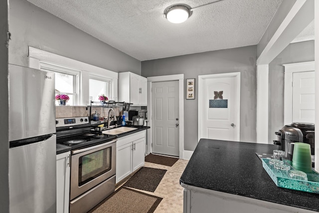 2745 Columbus Ave, Minneapolis, MN 55407 - kitchen featuring appliances with stainless steel finishes, a sink, dark countertops, white cabinetry, and a textured ceiling