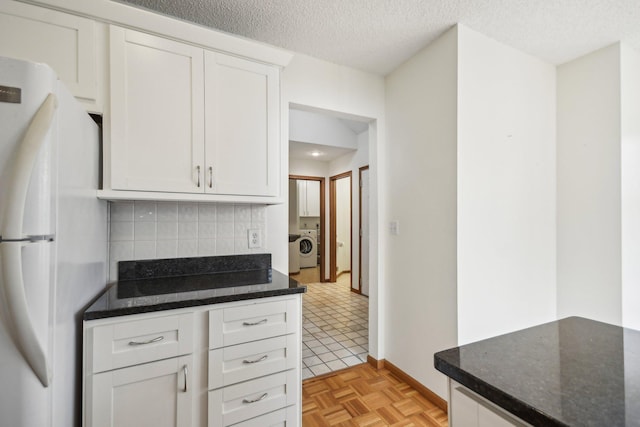 4311 Pond View Dr, White Bear Twp, MN 55110 - kitchen with freestanding refrigerator, backsplash, white cabinetry, dark stone counters, and washer / dryer