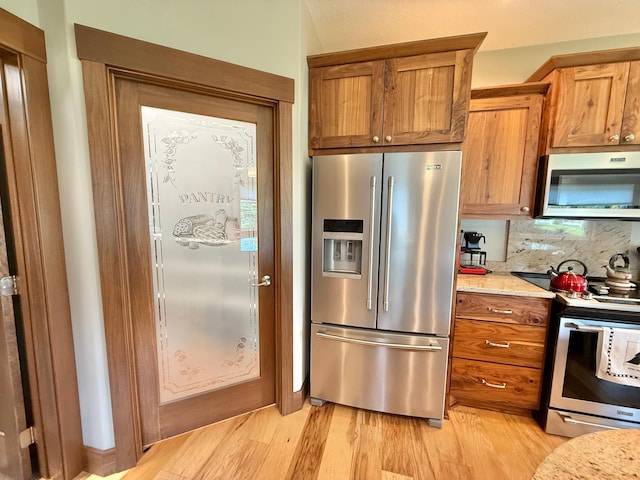 910 Lake Forest Cir, Detroit Lakes, MN 56501 - kitchen featuring appliances with stainless steel finishes, brown cabinets, light wood-style flooring, and decorative backsplash