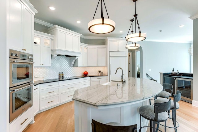 677 Shawnee Woods Rd, Medina, MN 55340 - kitchen featuring double oven, beverage cooler, white cabinets, ornamental molding, and recessed lighting