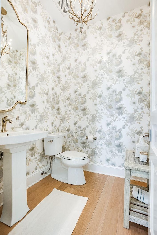677 Shawnee Woods Rd, Medina, MN 55340 - bathroom featuring wood finished floors, wallpapered walls, toilet, a chandelier, and baseboards