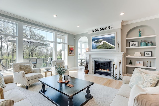 677 Shawnee Woods Rd, Medina, MN 55340 - living room featuring ornamental molding, arched walkways, a fireplace, wood finished floors, and built in shelves