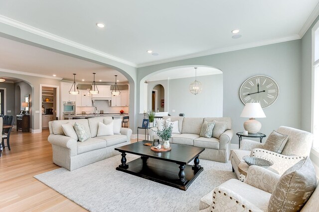 677 Shawnee Woods Rd, Medina, MN 55340 - living area featuring arched walkways, light wood-style flooring, recessed lighting, baseboards, and crown molding