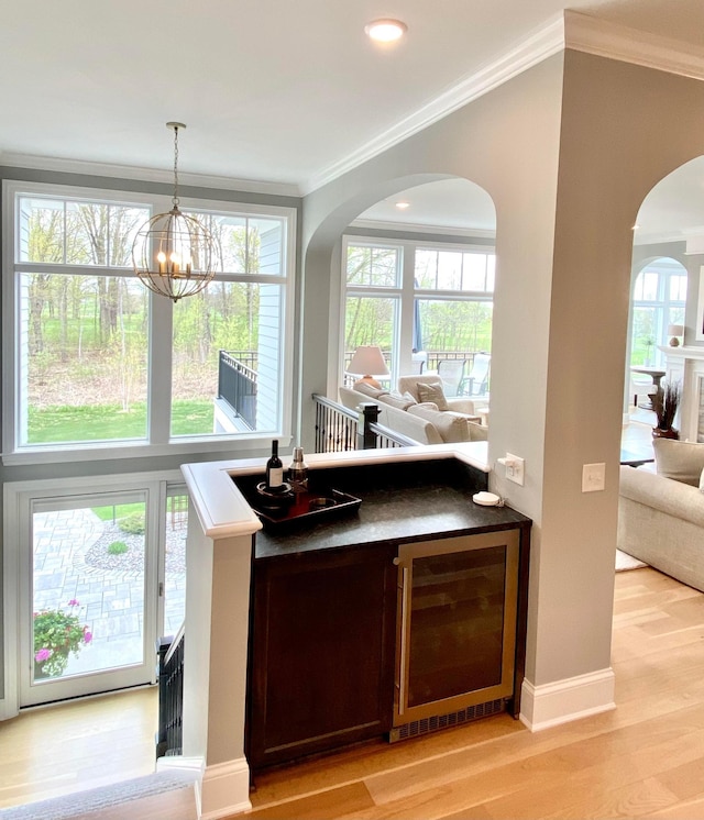 677 Shawnee Woods Rd, Medina, MN 55340 - bar featuring beverage cooler, arched walkways, light wood-type flooring, a chandelier, and plenty of natural light