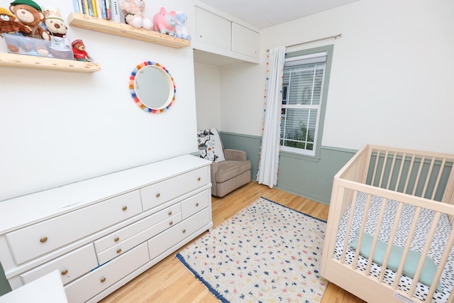 1423 Cedar St, Alexandria, MN 56308 - bedroom featuring a wainscoted wall, a crib, and light wood-style flooring
