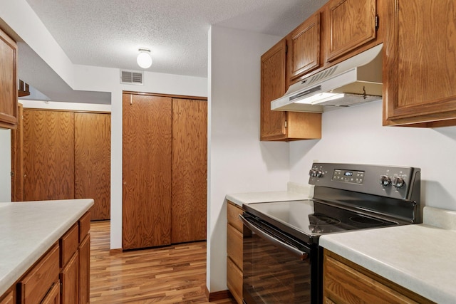 1225 Ferndale St N Unit B16, Maplewood, MN 55119 - kitchen with black electric range, under cabinet range hood, light wood-style floors, brown cabinetry, and light countertops