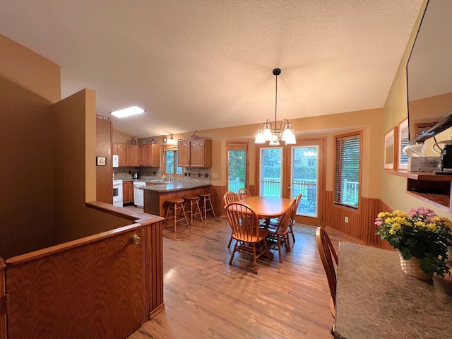 1715 Hansen Dr SW, Willmar, MN 56201 - dining area featuring vaulted ceiling, light wood-style flooring, healthy amount of natural light, a wainscoted wall, and a chandelier