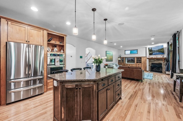 6415 Queensland Ln N, Maple Grove, MN 55311 - kitchen featuring appliances with stainless steel finishes, arched walkways, light wood-type flooring, a fireplace, and dark stone counters