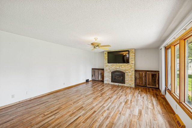 2216 146th Ave NE, Ham Lake, MN 55304 - unfurnished living room with light wood finished floors, a textured ceiling, a fireplace, and a ceiling fan