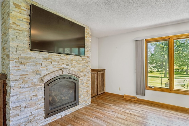 2216 146th Ave NE, Ham Lake, MN 55304 - unfurnished living room featuring a textured ceiling, light wood-style flooring, and a stone fireplace