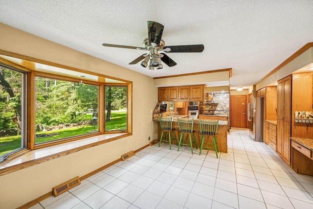 2216 146th Ave NE, Ham Lake, MN 55304 - kitchen featuring stainless steel appliances, a peninsula, a ceiling fan, brown cabinetry, and a kitchen bar