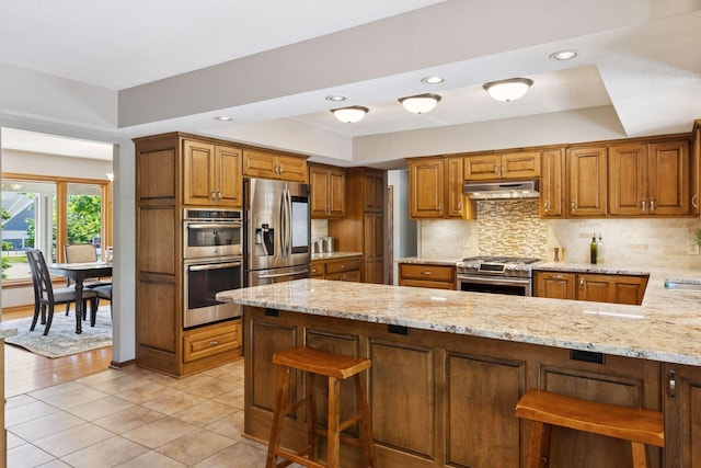 15905 43rd Ave N, Plymouth, MN 55446 - kitchen with appliances with stainless steel finishes, under cabinet range hood, light stone counters, tasteful backsplash, and brown cabinets