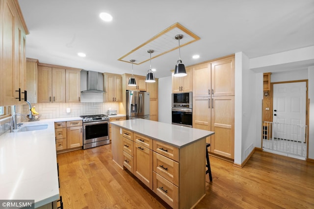 2119 13th Ave E, North Saint Paul, MN 55109 - kitchen featuring stainless steel appliances, wall chimney exhaust hood, light brown cabinets, a center island, and light wood finished floors