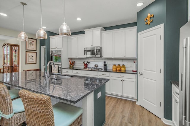 4745 Copper Cir, Woodbury, MN 55129 - kitchen featuring appliances with stainless steel finishes, a breakfast bar, light wood finished floors, decorative backsplash, and white cabinets