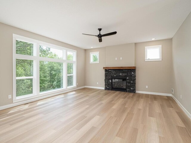 20713 Tamarack St NW, Oak Grove, MN 55011 - unfurnished living room featuring a ceiling fan, light wood-style floors, a stone fireplace, baseboards, and healthy amount of natural light