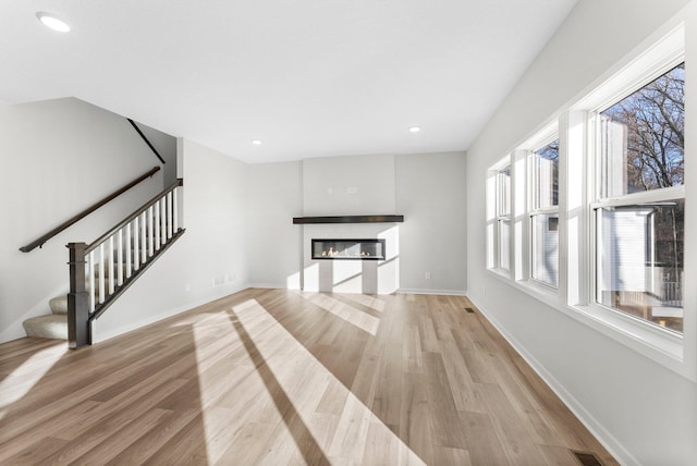 1708 Misty Cir, Buffalo, MN 55313 - unfurnished living room featuring plenty of natural light, stairs, light wood-style floors, a glass covered fireplace, and recessed lighting