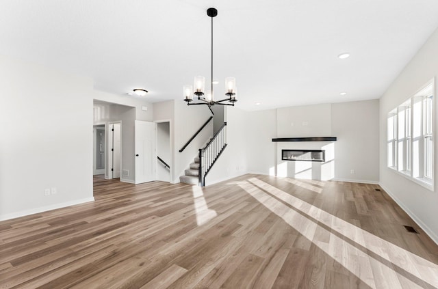 1708 Misty Cir, Buffalo, MN 55313 - unfurnished living room with light wood-style flooring, a chandelier, a glass covered fireplace, stairway, and baseboards