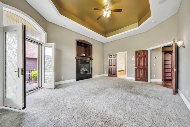 18141 87th Ave N, Maple Grove, MN 55311 - unfurnished living room featuring a glass covered fireplace, carpet floors, a tray ceiling, ceiling fan, and baseboards