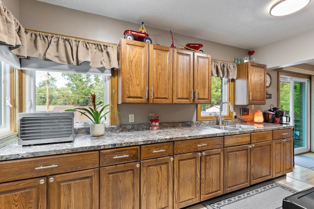 2196 Waukon Ave, Saint Paul, MN 55119 - kitchen with a sink, brown cabinetry, a textured ceiling, light tile patterned flooring, and light stone countertops
