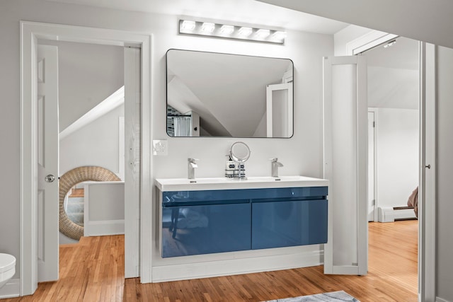 3812 Elliot Ave, Minneapolis, MN 55407 - bathroom with a baseboard heating unit, wood finished floors, double vanity, and toilet