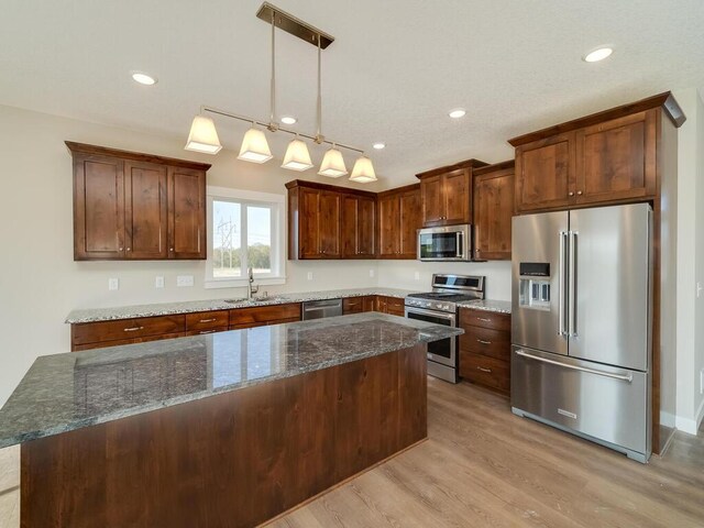 967 206th Ave NW, Oak Grove, MN 55011 - kitchen with appliances with stainless steel finishes, a sink, light wood-type flooring, dark stone countertops, and decorative light fixtures