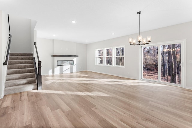 17720 Lincoln St NW, Elk River, MN 55330 - unfurnished living room with a glass covered fireplace, a chandelier, light wood-style floors, stairs, and baseboards