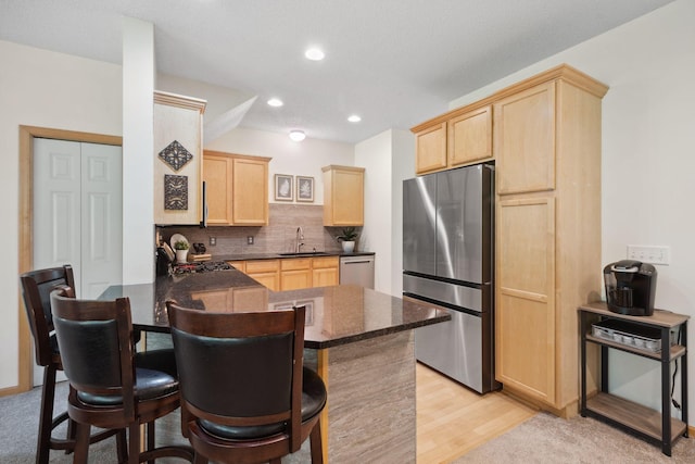 2658 133rd St W, Rosemount, MN 55068 - kitchen featuring appliances with stainless steel finishes, light brown cabinetry, a sink, a peninsula, and a kitchen bar
