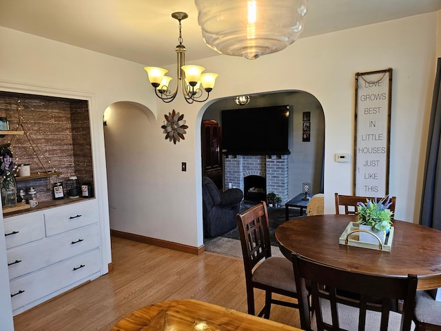 205 2nd Ave W, Lamberton, MN 56152 - dining space featuring arched walkways, light wood-type flooring, a brick fireplace, a chandelier, and baseboards