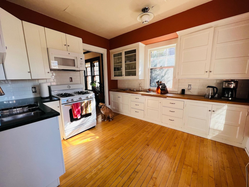 928 Franklin Ter, Minneapolis, MN 55406 - kitchen featuring white appliances, decorative backsplash, white cabinetry, light wood-style floors, and glass insert cabinets