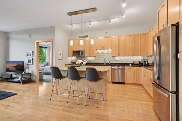 215 10th Ave S Unit 312, Minneapolis, MN 55415 - kitchen featuring appliances with stainless steel finishes, light brown cabinets, a kitchen breakfast bar, light wood-type flooring, and backsplash