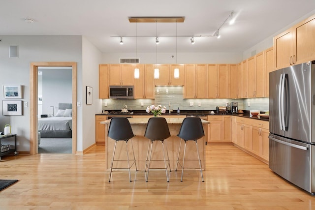 215 10th Ave S Unit 312, Minneapolis, MN 55415 - kitchen with stainless steel appliances, light brown cabinetry, a sink, a kitchen bar, and light wood-style floors