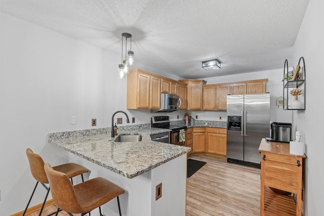 1297 124th Ave NE, Blaine, MN 55434 - kitchen with appliances with stainless steel finishes, a peninsula, light stone counters, a kitchen breakfast bar, and light wood-type flooring