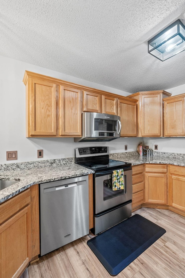 1297 124th Ave NE, Blaine, MN 55434 - kitchen with stainless steel appliances, a textured ceiling, light wood finished floors, and light stone counters