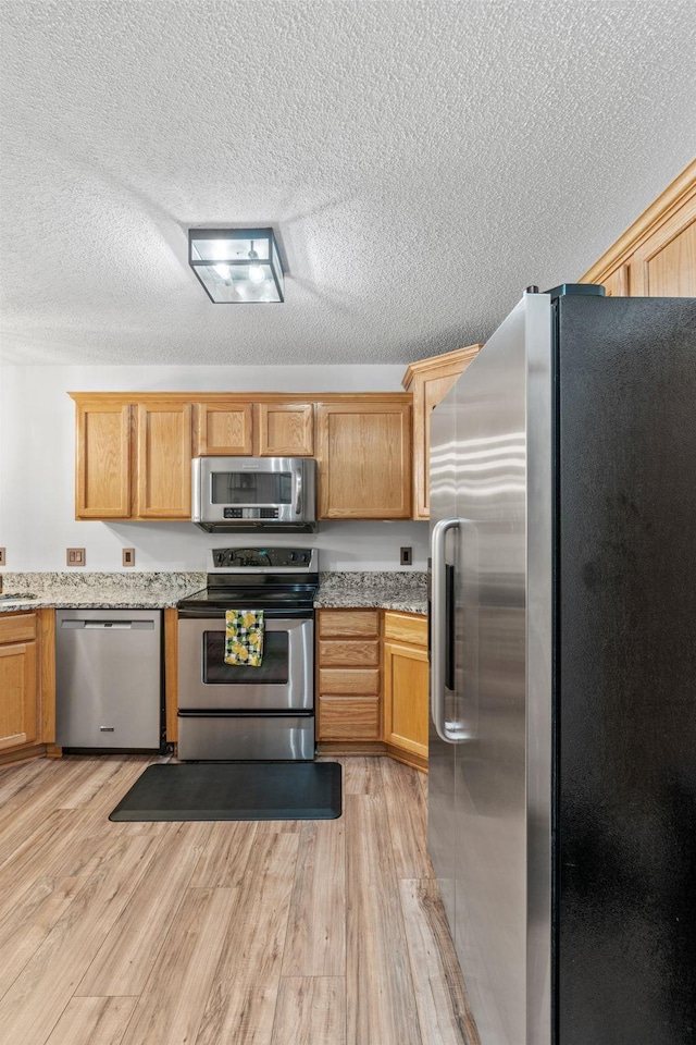 1297 124th Ave NE, Blaine, MN 55434 - kitchen with stainless steel appliances, light wood finished floors, a textured ceiling, and light stone counters