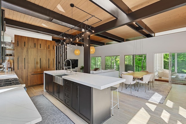18101 Woolman Dr, Minnetonka, MN 55345 - kitchen with a sink, wooden ceiling with exposed beams, light wood-type flooring, light countertops, and a center island with sink
