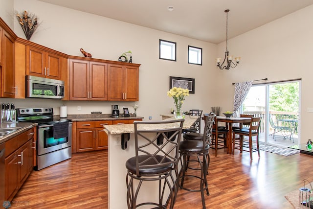 4110 Clubhouse Dr S, Fargo, ND 58104 - kitchen with stainless steel appliances, brown cabinetry, a kitchen bar, wood finished floors, and a chandelier