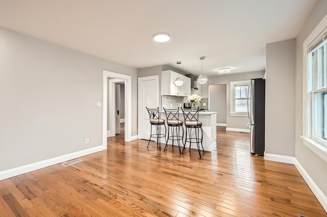 4245 11th Ave S, Minneapolis, MN 55407 - kitchen with freestanding refrigerator, a peninsula, a kitchen bar, white cabinets, and light wood-style floors