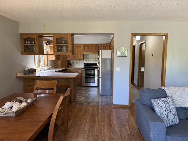 507 Pine Ridge Ter, River Falls, WI 54022 - kitchen featuring stainless steel appliances, brown cabinetry, a peninsula, decorative backsplash, and glass insert cabinets