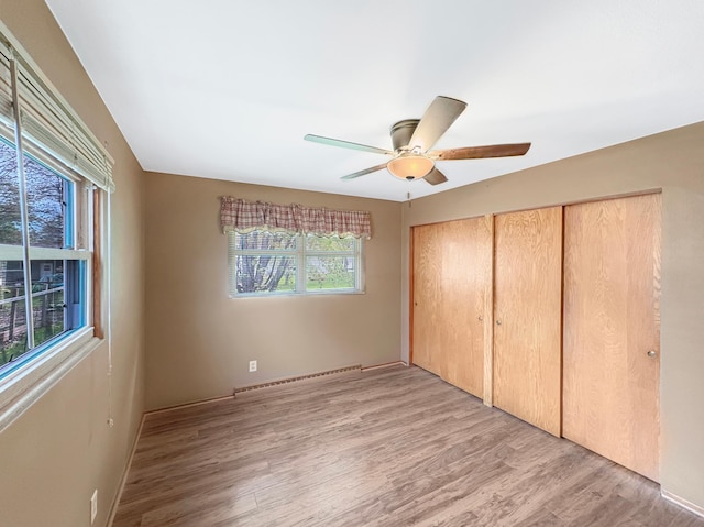 602 26th St, Scanlon, MN 55720 - unfurnished bedroom featuring a baseboard heating unit, light wood finished floors, baseboards, a ceiling fan, and two closets